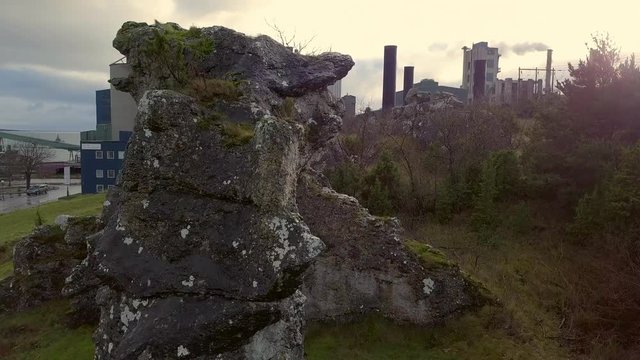 Drone shot of "rauk" rock formation in front of industry factory buildings. Aerial view, nature vs industrial background, air pollution, climate change, global warming. Gotland, Sweden, 4K resolution
