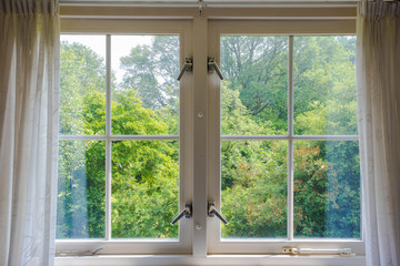 Beautiful cozy window with green forest view and white curtains.