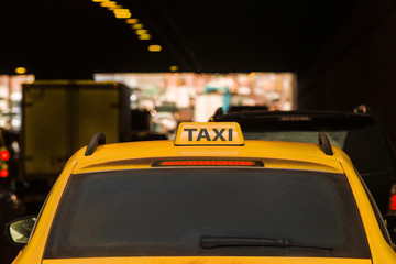Yellow taxi moves in the midst of cars along city streets.