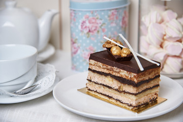 Chocolate cake with nuts on a plate near a cup, teapot and jar of marshmallows.