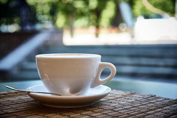 White cup with coffee drink on bamboo napkin close-up on bright background with bokeh.