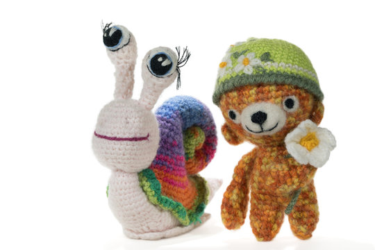 Crochet rainbow snail with eyes and crochet bear wearing a hat with a flower, on white background. Amigurumi. Handmade