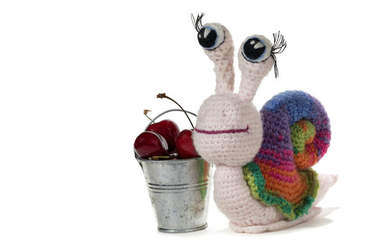 Crochet rainbow snail with eyes and metal bucket with cherries, on white background. Amigurumi. Handmade