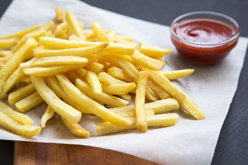 French fries with ketchup over black background, side view. Closeup.