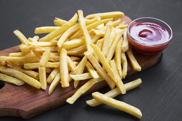 French fries with ketchup over black background. Side view.