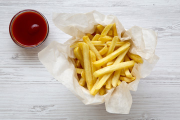 French fries with ketchup on a white wooden table, top view.
