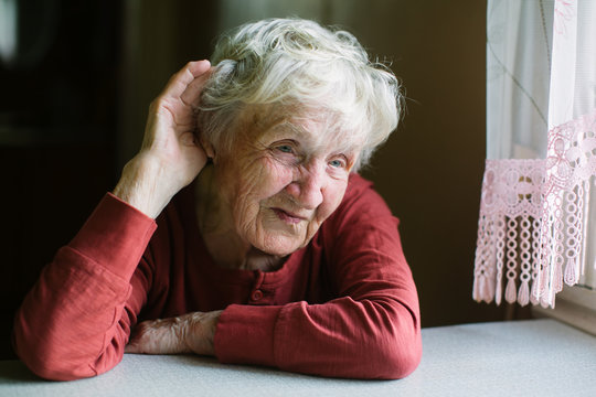 An elderly woman listens with her hand to her ear. Hard of hearing, seniors hearing loss.