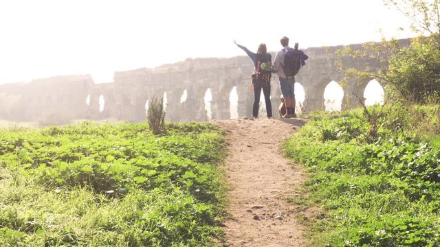 Young lovely couple backpackers tourists reading map pointing directions roman aqueduct arches in parco degli acquedotti park ruins in rome on romantic misty sunrise with guitar and sleeping bag slow