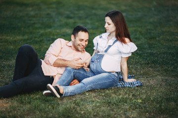 Naklejka na ściany i meble Family conversation. Father talking to his unborn child. Pregnant couple sitting in the park chatting. Relations, maternity, family, parenthood, love concept