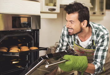 Portrait of smiling man holding tray of bakes in kitchen at home.