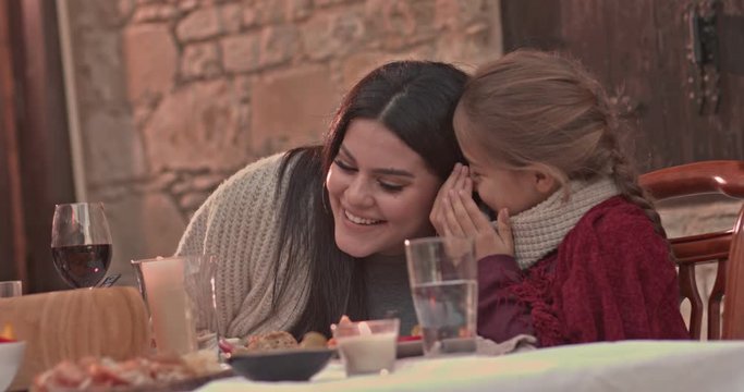Young daughter whispering secrets in mother's ear at lunch