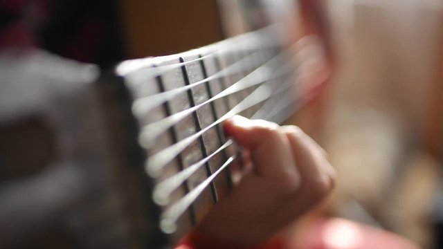 Teen girl playing guitar at home. Close up of cute teen indoors in a hoody softly strumming her guitar.