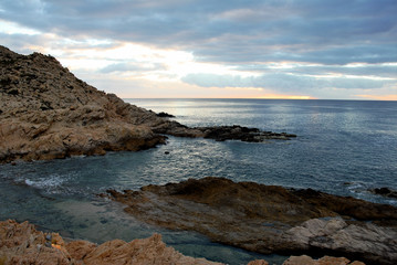 ocean and tide pool on rocky coastline with gray clouds above orange horizon