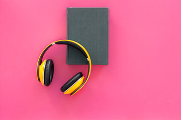 Distance education, e-learning concept. Headphones near hardback book with empty cover on pink background top view copy space
