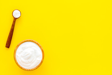 Healthy product, healthy meal. Greek yogurt in brown bowl near spoon on yellow background top view copy space