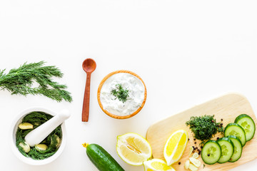 Greek yogurt as salad dressing. Bowl with yogurt, greenery, cucumber, oranges on cutting board on white kitchen desk top view copy space