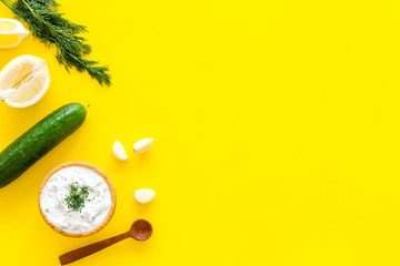 Greek yogurt dip with greenery, cucumber, oranges, garlic on yellow background top view copy space