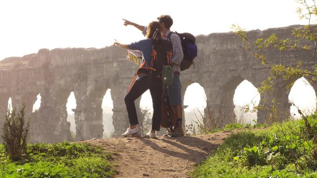 Young lovely couple backpackers tourists reading map pointing directions roman aqueduct arches in parco degli acquedotti park ruins in rome on romantic misty sunrise with guitar and sleeping bag slow