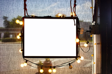 Blank hanging sign surrounded by party lights in shop window with semi-transparent dark solar...