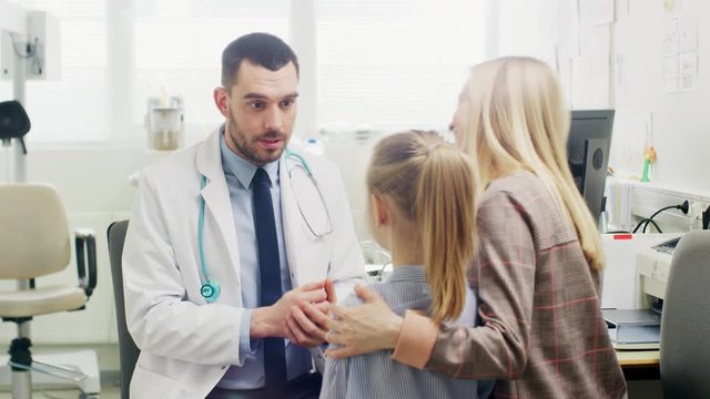 Friendly Doctor Does Routine Examination of a Sweet Little Girl who Came with Her Mother. Pediatrician Talks to Both of them. Doctor's Office is Bright and Modern.