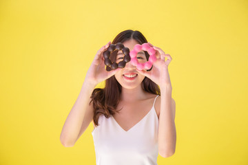 Attractive Asian woman holding two donuts with cute smiling expression over yellow background