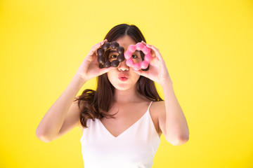 Attractive Asian woman holding two donuts with cute smiling expression over yellow background