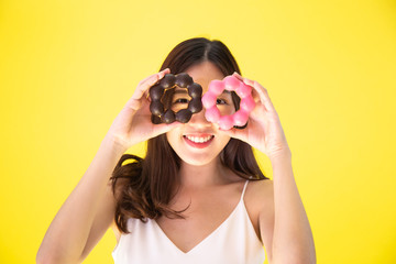 Attractive Asian woman holding two donuts with cute smiling expression over yellow background