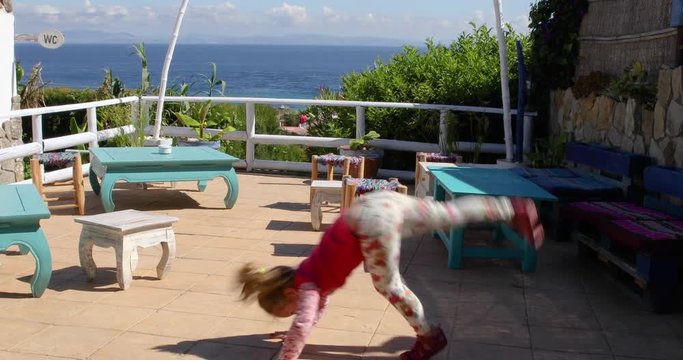four years old blonde happy girl trying to do the somersault or handstand in exterior roof
