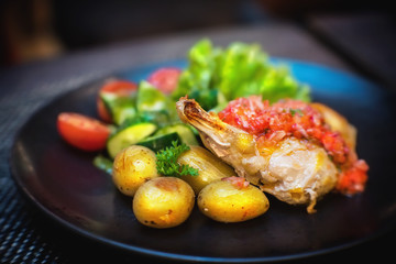 Fried chicken with potatos and vegetables on a black plate.