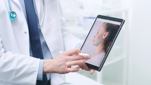 Plastic / Cosmetic Surgeon Holds Digital Tablet Computer, on Screen it Shows Types of Facelift, Forehead Lift, Cheek Bones and Nose Correcting Procedures Available for Women. 