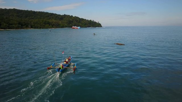 Aerial tracking video of a classic Indonesian fishing boat sailing towards a popular beach in Pangandaran