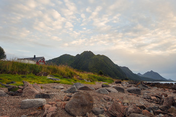 Red house on the shore with view to mountain and sunset on the sea in the Norway at summer
