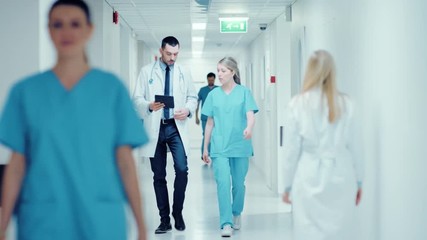 Surgeon and Female Doctor Walk Through Hospital Hallway, They Consult Digital Tablet Computer while Talking about Patient's Health. Shot on RED EPIC-W 8K Helium Cinema Camera. - Powered by Adobe