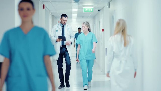 Surgeon and Female Doctor Walk Through Hospital Hallway, They Consult Digital Tablet Computer while Talking about Patient's Health. Shot on RED EPIC-W 8K Helium Cinema Camera.