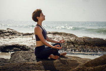The girl is meditating on the rocks. Yoga on the beach.
