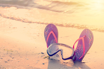 Summer holiday concept. Colorful flip flops with diving mask on the sandy beach during sunset. Toned