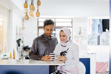 A young Muslim Malay couple sit at a table top counter and enjoy a coffee early in the morning when they break fast. 