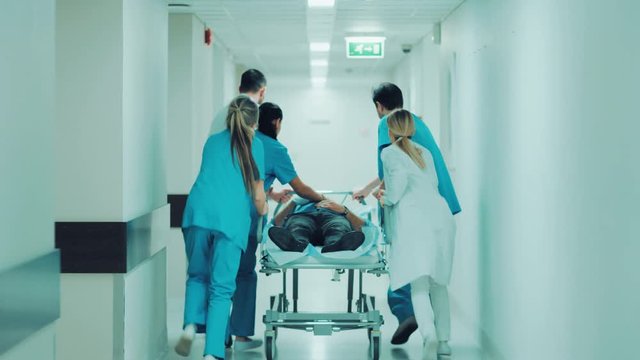 Emergency Department: Doctors, Nurses and Paramedics Push Gurney / Stretcher with Seriously Injured Patient towards the Operating Room. Shot on RED EPIC-W 8K Helium Cinema Camera.