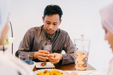 Fototapeta na wymiar Image of a Malay Muslim man at the dining table before Ramadan. He is having breakfast with his wife and he is young,handsome and a traditional garb .