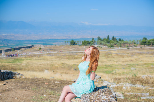 Girl tourist taking picture of Hierapolis in Turkey, Pamukkale, beautiful landscape with ruin, trees and mountain, woman in lace summer dress  
