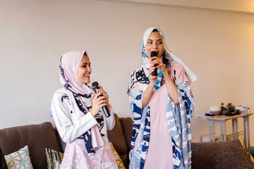 Two Muslim Malay women unwinding and relaxing as they enjoy singing in their Karaoke machine at home during the day during Raya. 