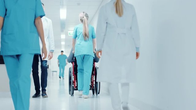 Following Shot of the Female Nurse Moving Patient in the Wheelchair Through the Hospital Corridor. Doing Procedures. Shot on RED EPIC-W 8K Helium Cinema Camera.