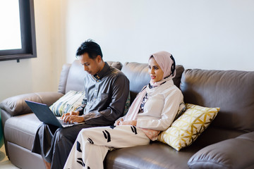 Portrait of a Malaysian Muslim couple at home during the Muslim festival of Hari Raya in Singapore, Asia. They are sitting on their home sofa and relaxing.
