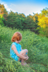 The girl is sitting on the edge of the forest