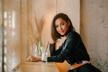 Portrait of a young, beautiful and fashionable Malay Muslim woman in a cafe. She is enjoying a drink on a weekend.