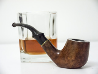 Briar smoking pipe with glass of whisky side view with distorted background