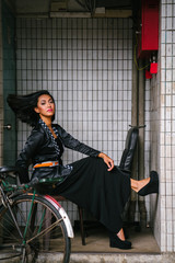 Fashion portrait of a young, slim, attractive and fashionable Muslim Malay woman sitting and posing on a chair in a city in Asia. 