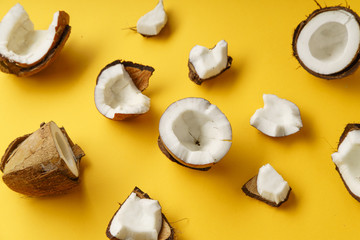 Cracked coconut and coconut pieces on yellow background. Overhead view