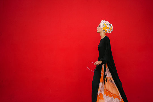 Portrait Of A Fashionable Muslim Woman Model In A Head Scarf Hijab Against A Red Background In A Studio. 