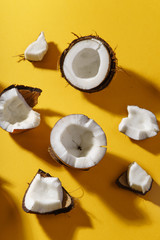Cracked coconut and coconut pieces on yellow background. Overhead view